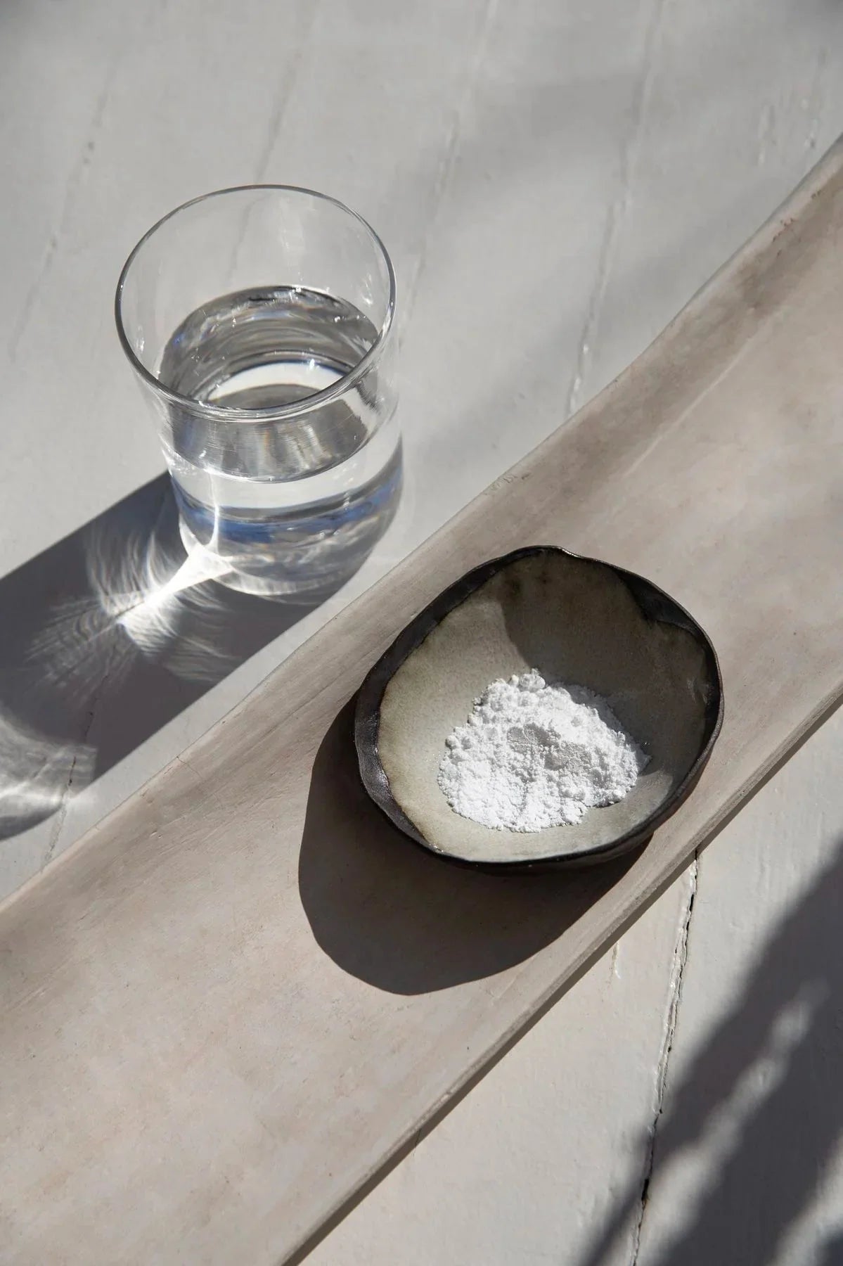 Creatina monohidrato en polvo en un cuenco junto a un vaso de agua
