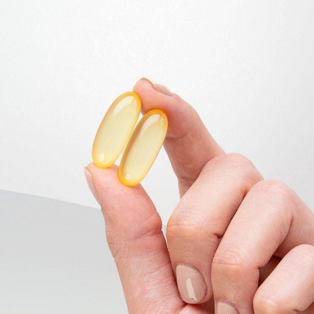 Mano sujetando dos perlas de omega 3 entre los dedos